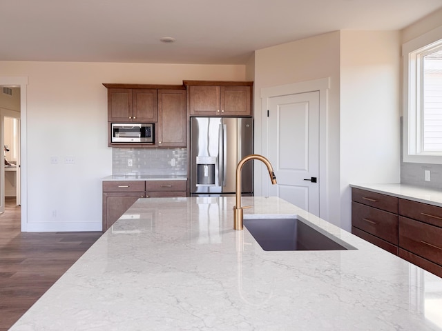 kitchen featuring light stone counters, stainless steel appliances, dark wood-type flooring, a sink, and decorative backsplash