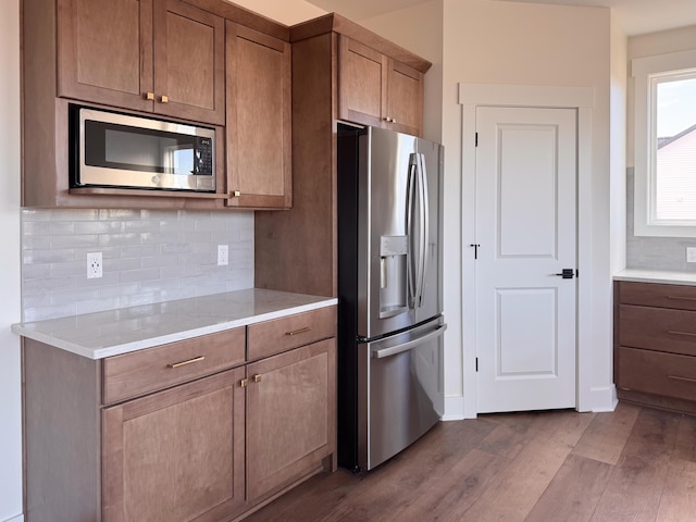 kitchen featuring dark wood finished floors, stainless steel appliances, light countertops, decorative backsplash, and brown cabinetry