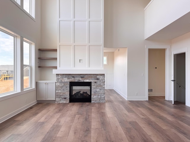 unfurnished living room with a high ceiling, baseboards, wood finished floors, and a stone fireplace