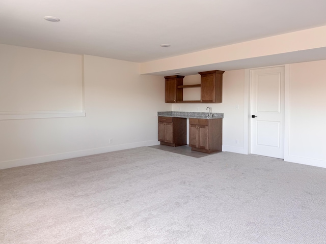 interior space featuring light colored carpet, a sink, and baseboards