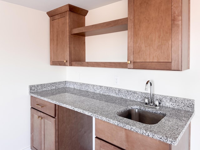 kitchen with light stone counters, a sink, and open shelves