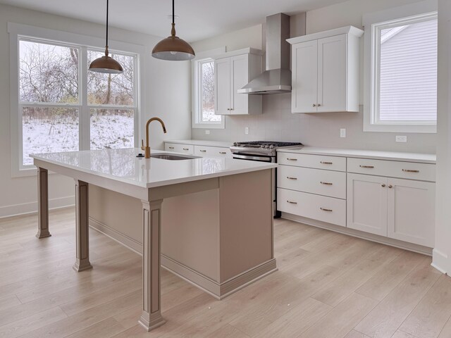 kitchen featuring stainless steel gas range, decorative light fixtures, wall chimney range hood, sink, and a center island with sink