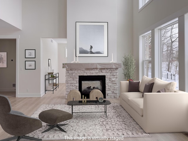 living room with light hardwood / wood-style flooring, a fireplace, plenty of natural light, and a high ceiling