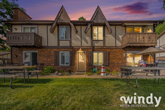 back of property with brick siding, a chimney, a balcony, and stucco siding