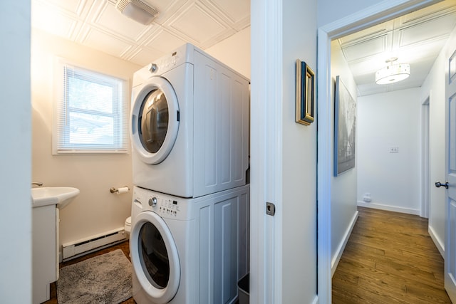 laundry area with sink, hardwood / wood-style flooring, a baseboard heating unit, and stacked washer / dryer