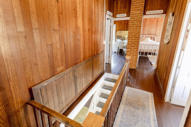 corridor with hardwood / wood-style floors, an upstairs landing, and wood walls