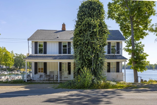 view of front facade featuring covered porch, board and batten siding, a chimney, and roof with shingles