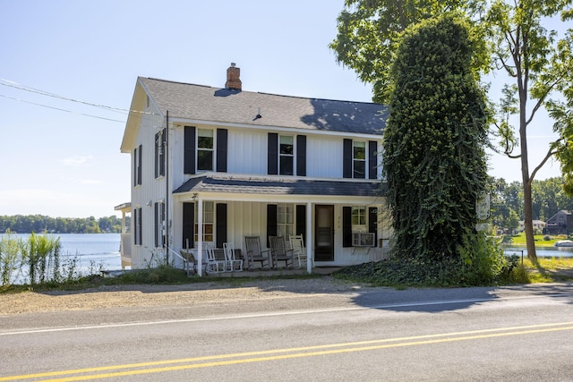 view of front of property featuring board and batten siding, roof with shingles, covered porch, cooling unit, and a chimney