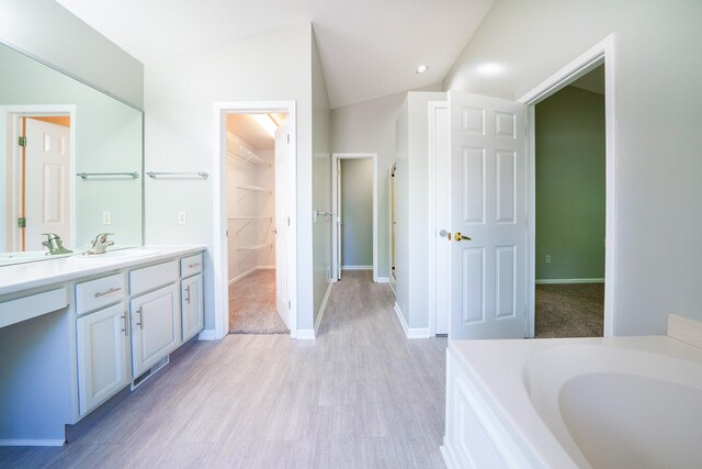 bathroom with vanity, vaulted ceiling, hardwood / wood-style floors, and a tub