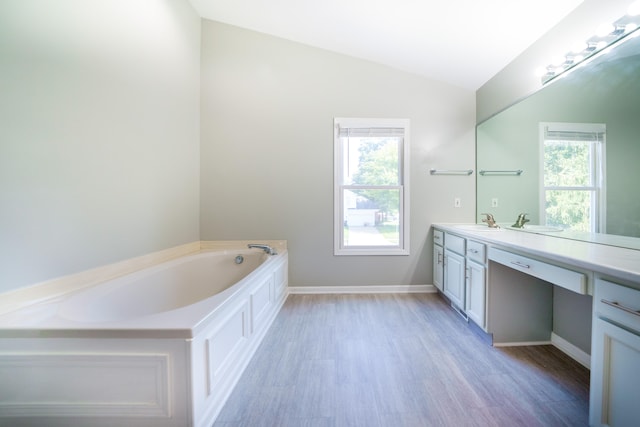 bathroom with lofted ceiling, a tub to relax in, vanity, and a healthy amount of sunlight