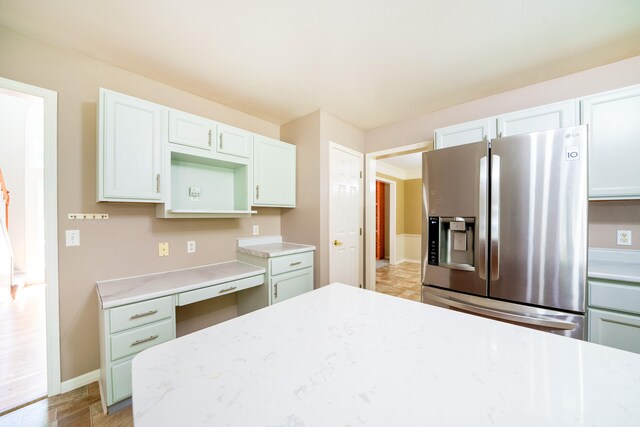 kitchen with stainless steel refrigerator with ice dispenser, built in desk, light stone countertops, and white cabinets