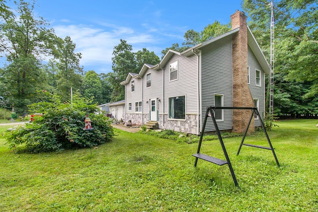 rear view of property featuring entry steps, a garage, stone siding, a lawn, and a chimney