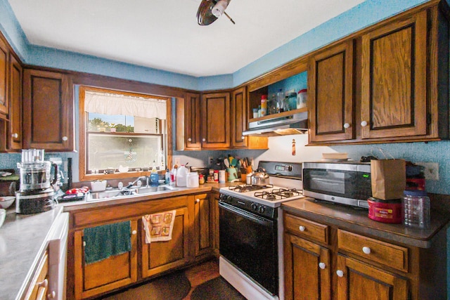 kitchen with brown cabinets, gas range oven, stainless steel microwave, a sink, and under cabinet range hood