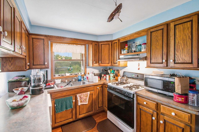 kitchen featuring stainless steel microwave, brown cabinets, gas range oven, under cabinet range hood, and a sink