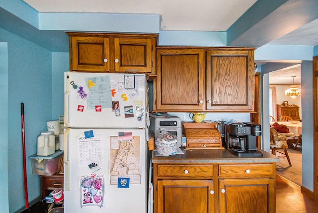 kitchen featuring dark countertops, a chandelier, brown cabinetry, and freestanding refrigerator