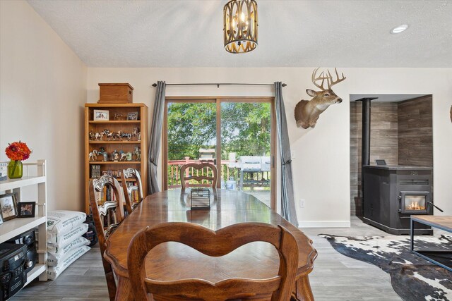 dining room with wood-type flooring, a notable chandelier, a textured ceiling, and a wood stove