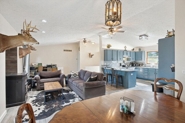 living room with a textured ceiling, ceiling fan with notable chandelier, lofted ceiling, and light hardwood / wood-style floors