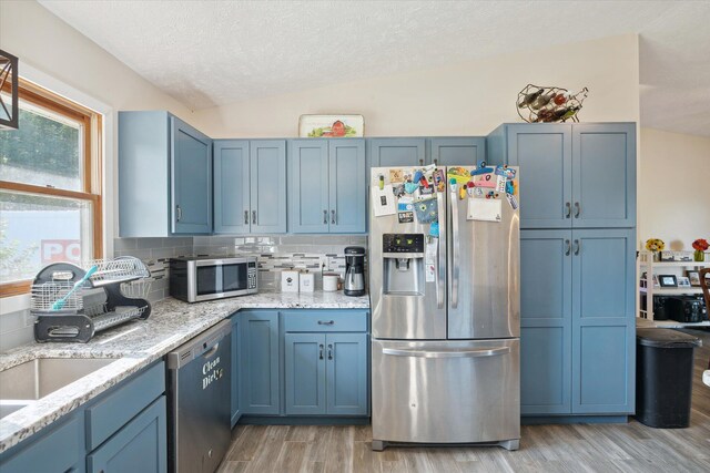 kitchen with stainless steel appliances, lofted ceiling, a textured ceiling, and light wood-type flooring