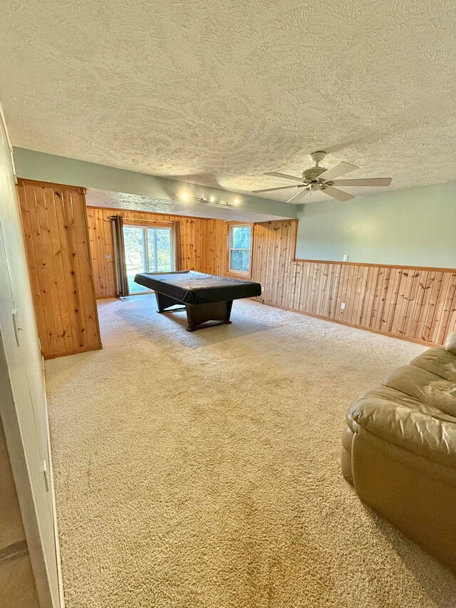 playroom with a textured ceiling, carpet flooring, wood walls, and ceiling fan