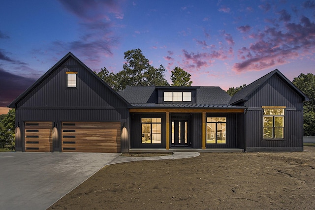 modern farmhouse featuring driveway, a standing seam roof, board and batten siding, an attached garage, and metal roof