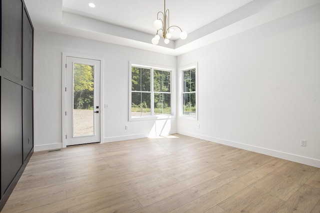 spare room with baseboards, a raised ceiling, a chandelier, and light wood finished floors