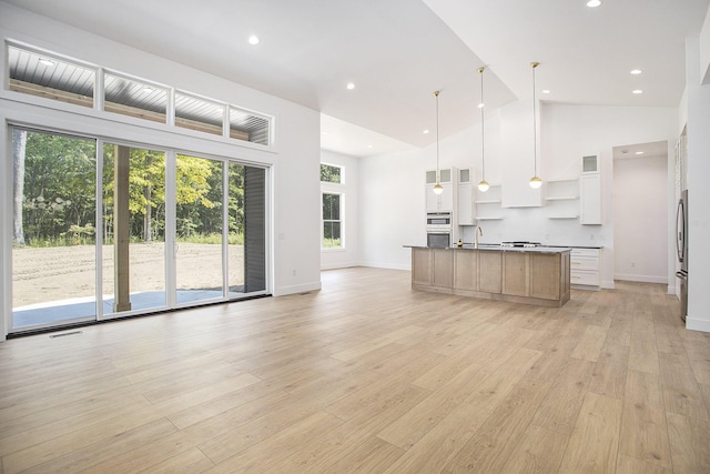 kitchen with visible vents, open floor plan, light wood-style flooring, high vaulted ceiling, and a kitchen island with sink