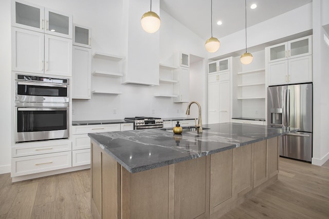 kitchen with light wood finished floors, open shelves, a center island with sink, appliances with stainless steel finishes, and a sink