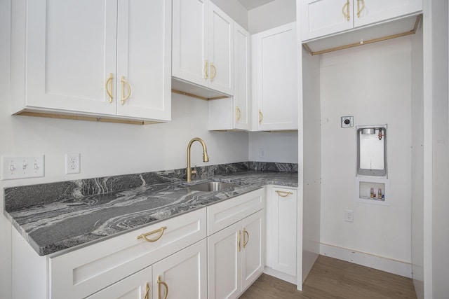 kitchen featuring baseboards, dark stone counters, wood finished floors, white cabinetry, and a sink