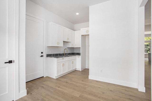 kitchen featuring a sink, dark stone countertops, light wood-style floors, white cabinets, and baseboards