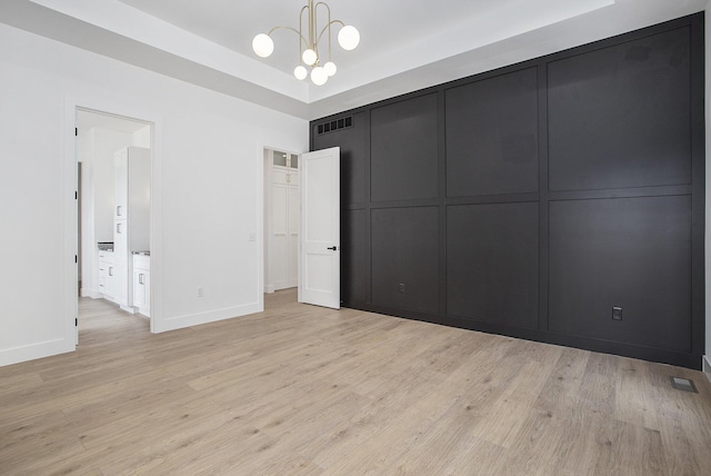 unfurnished bedroom featuring a raised ceiling, a decorative wall, baseboards, and light wood-type flooring