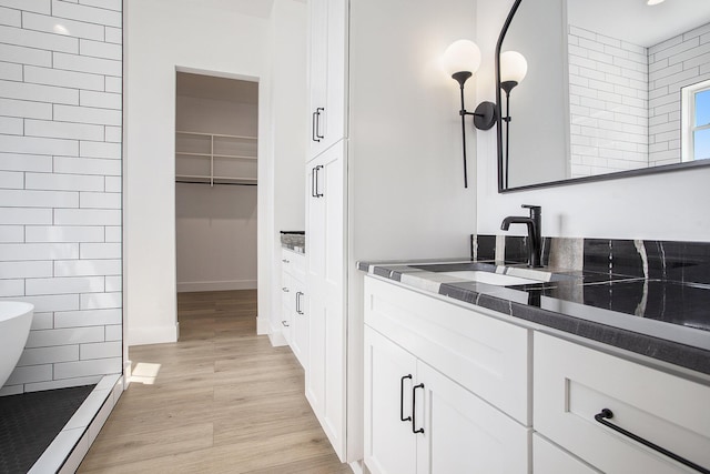 bathroom with wood finished floors, vanity, tile walls, a soaking tub, and a spacious closet