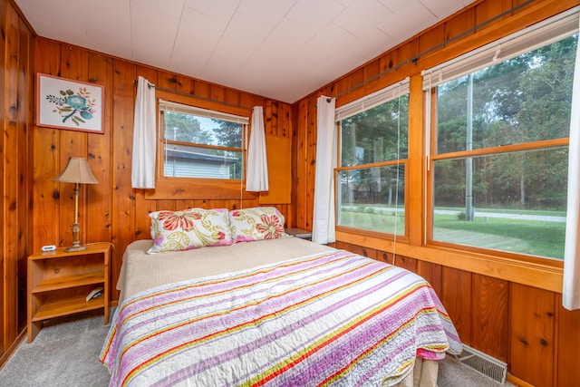 carpeted bedroom featuring multiple windows and wood walls