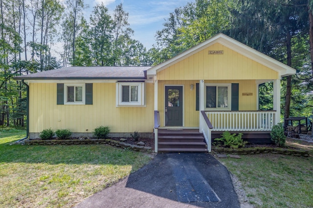 view of front of house with a porch, a front yard, and a shingled roof