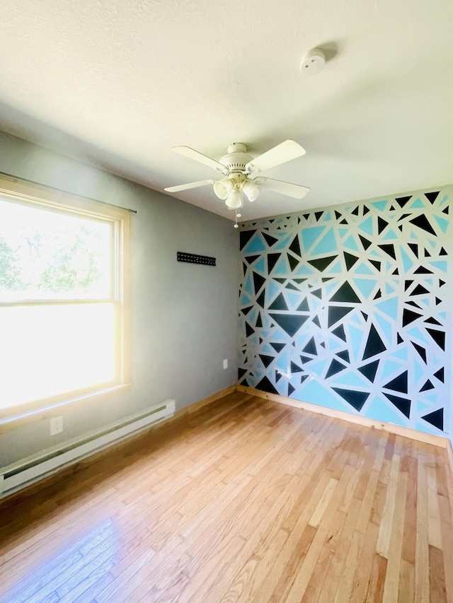 empty room with a ceiling fan, baseboard heating, and wood finished floors