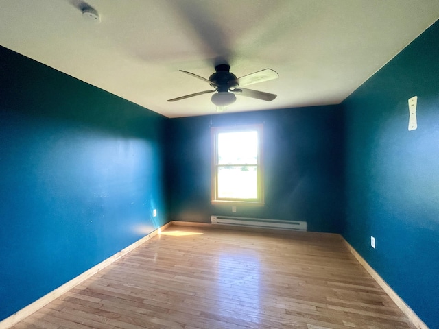 spare room featuring a ceiling fan, baseboards, a baseboard heating unit, and wood finished floors