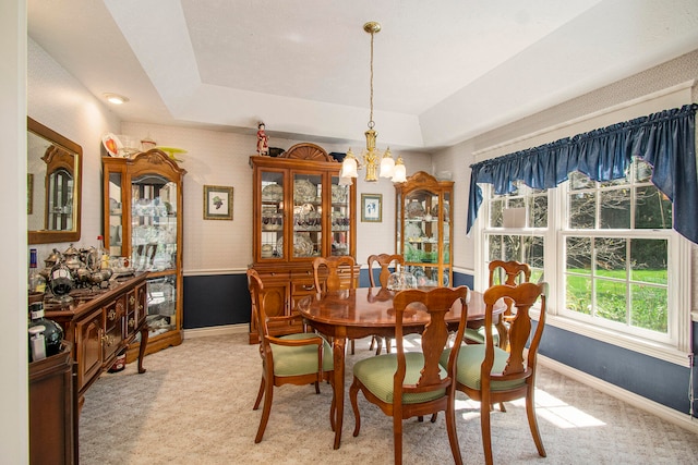 carpeted dining space with a chandelier and a raised ceiling