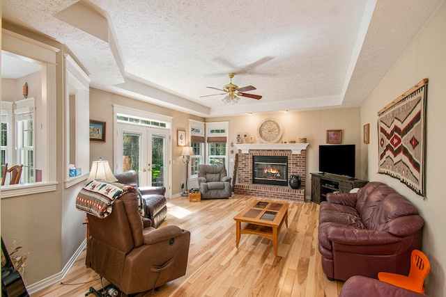 living room featuring french doors, light hardwood / wood-style floors, a textured ceiling, a tray ceiling, and a fireplace