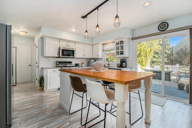 kitchen featuring appliances with stainless steel finishes, a kitchen bar, decorative backsplash, white cabinetry, and wooden counters