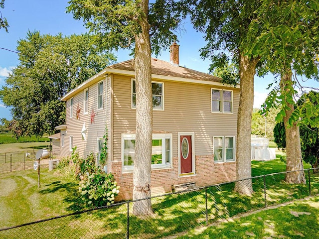 view of front of home featuring brick siding, fence private yard, a chimney, and a front lawn