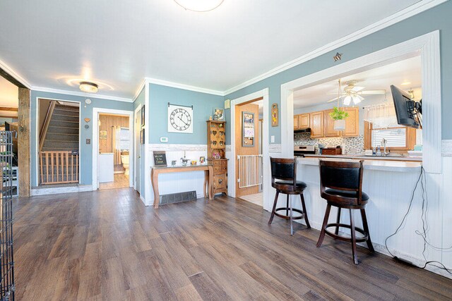 kitchen featuring light brown cabinets, tasteful backsplash, wood-type flooring, a kitchen bar, and crown molding