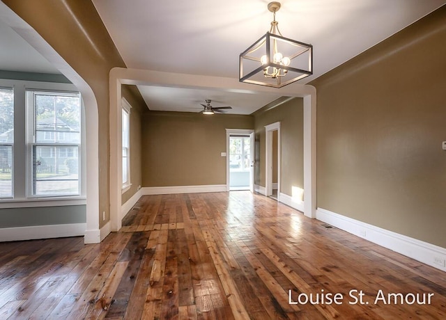 empty room featuring ceiling fan with notable chandelier, hardwood / wood-style flooring, and baseboards