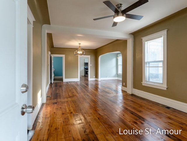 interior space with baseboards, visible vents, arched walkways, hardwood / wood-style flooring, and ceiling fan with notable chandelier