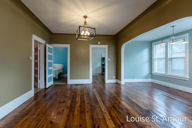 unfurnished dining area with an inviting chandelier, baseboards, arched walkways, and dark wood-style flooring
