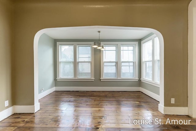 empty room with arched walkways, hardwood / wood-style flooring, and baseboards