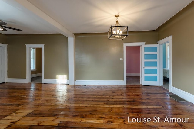 empty room featuring wood-type flooring, visible vents, baseboards, and ceiling fan with notable chandelier