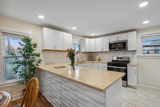 kitchen featuring decorative backsplash, white cabinetry, light stone counters, kitchen peninsula, and stainless steel appliances