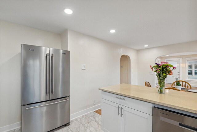 kitchen featuring light tile patterned floors, stainless steel appliances, light stone countertops, and white cabinets