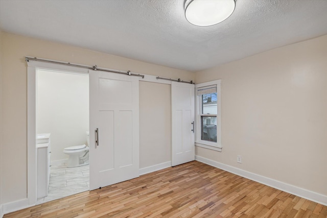 unfurnished bedroom with a textured ceiling, light hardwood / wood-style flooring, ensuite bathroom, and a barn door