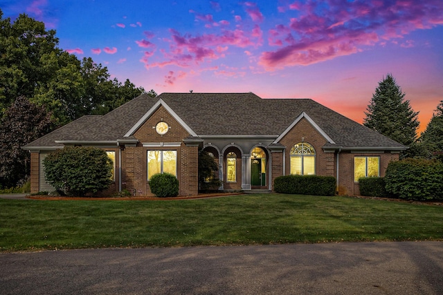 view of front facade featuring a shingled roof, brick siding, and a yard