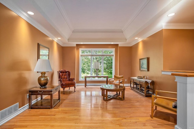 living area with light wood finished floors, baseboards, visible vents, a raised ceiling, and ornamental molding